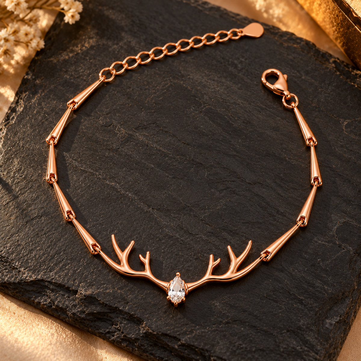 Rose gold antler bracelet lying on a matte black slate surface with warm gold lighting accents.