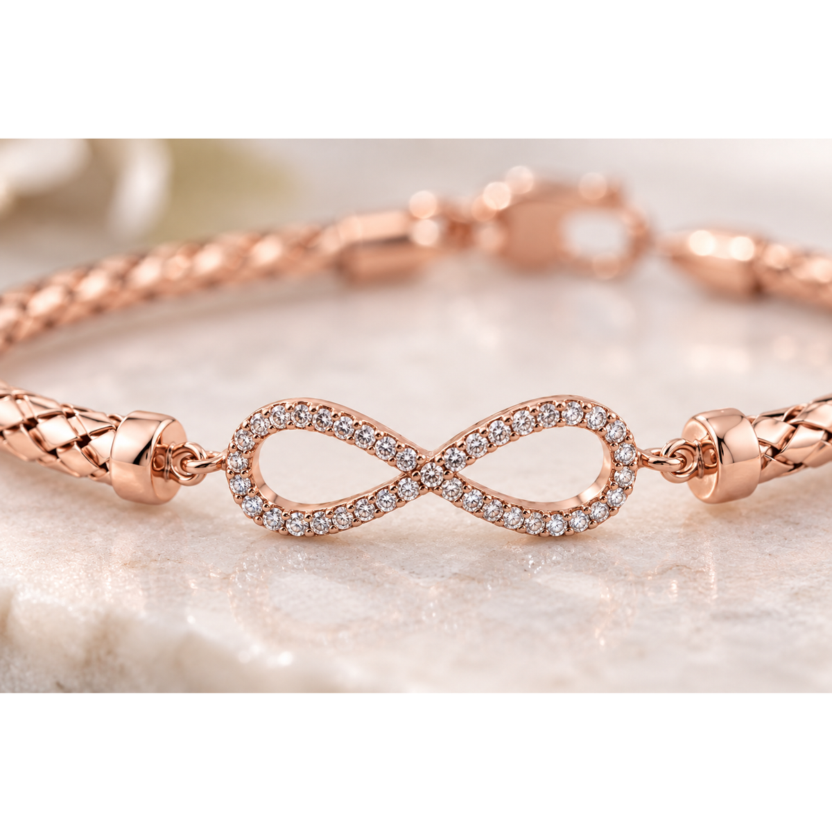 Macro detail of pave cubic zirconia infinity emblem on rose gold woven mesh bracelet.