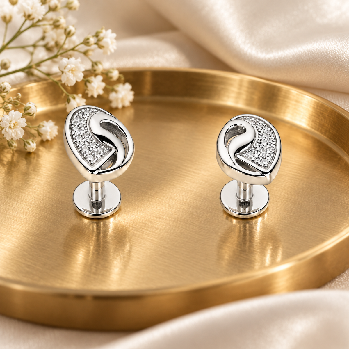 Silver clover earrings displayed on a gold tray with delicate white flowers and silk.