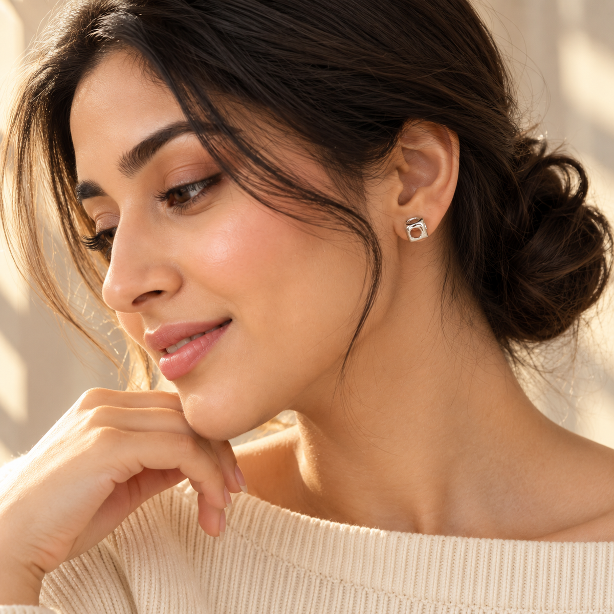 Profile view of a woman wearing a minimalist silver cube stud earring with her hair in a low bun.