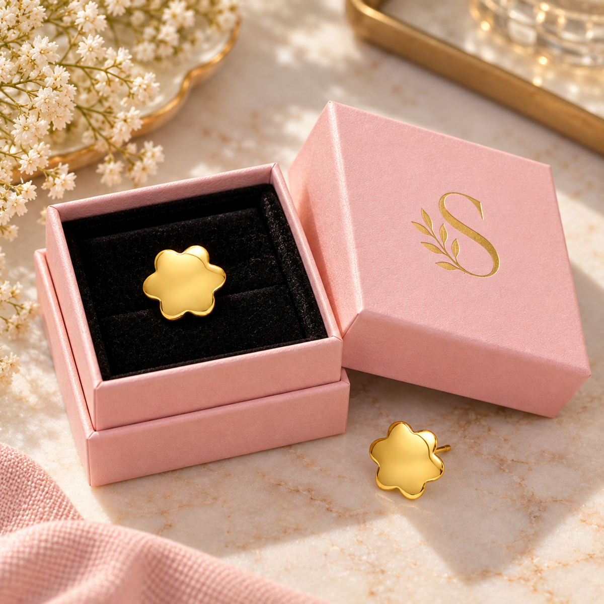 Gold blossom stud earring inside a pale pink Silvanya box on black velvet.