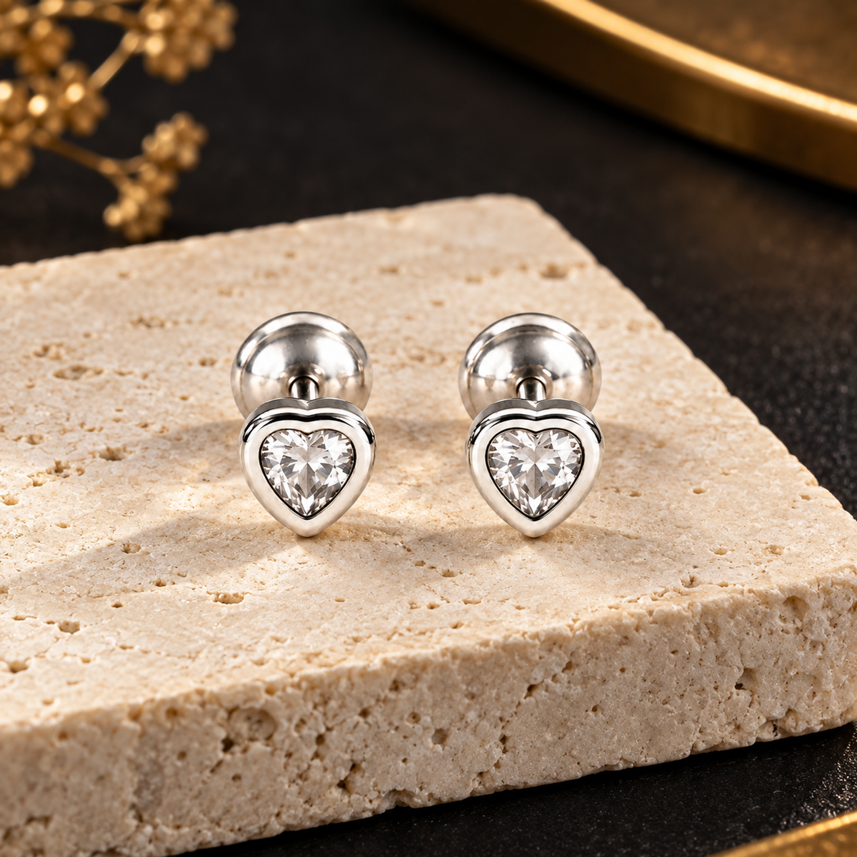 Silver heart stud earrings resting on an ivory stone pedestal against a matte black background.