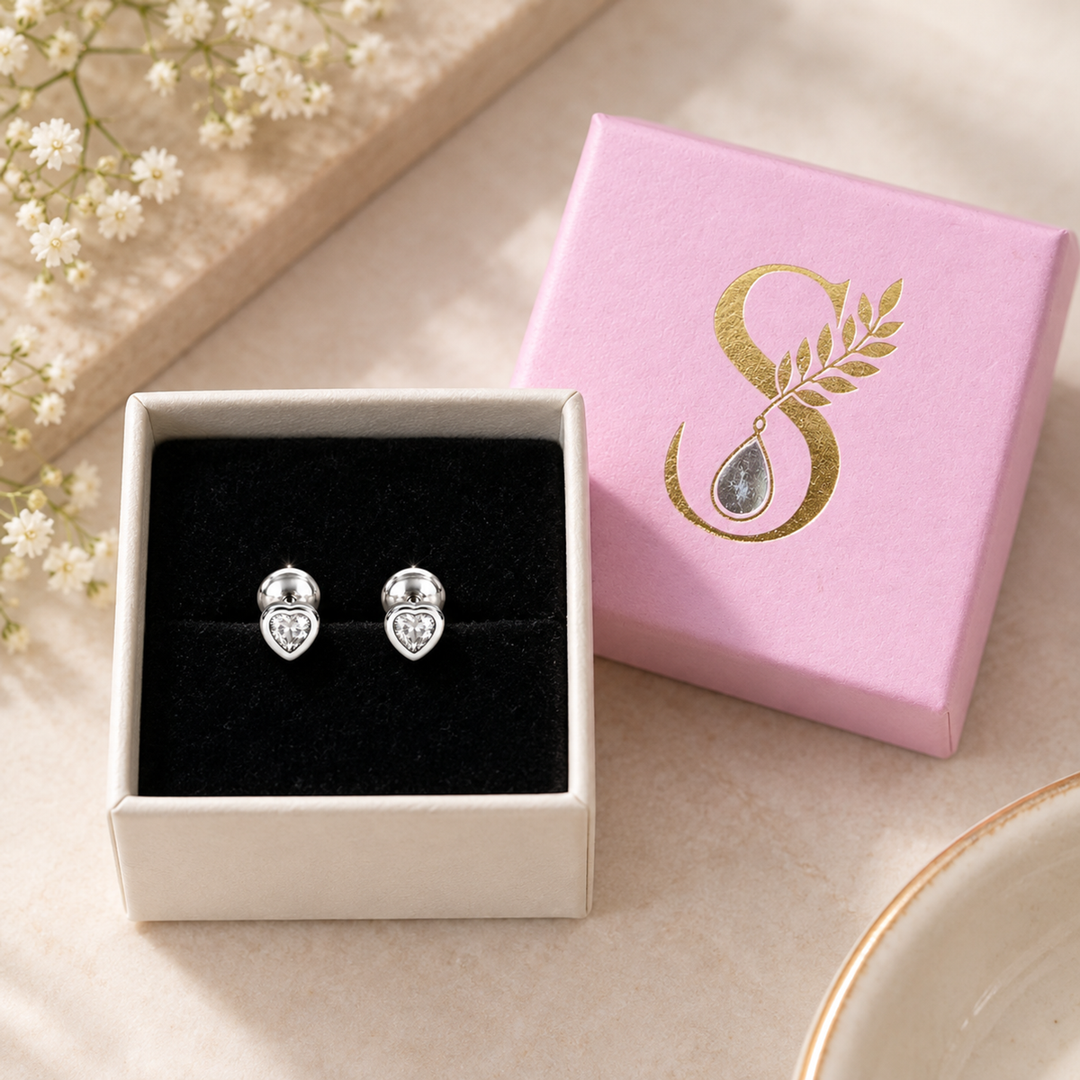 Silver heart stud earrings nestled in Silvanya's pale pink gift box with black velvet lining.