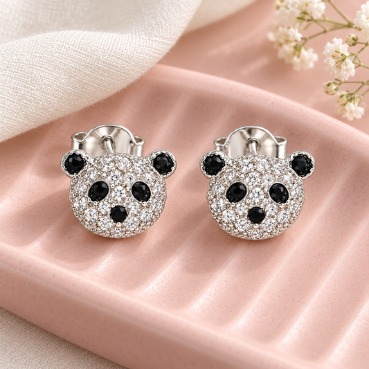 Silver panda studs displayed on a blush pink ceramic tray beside ivory silk fabric.