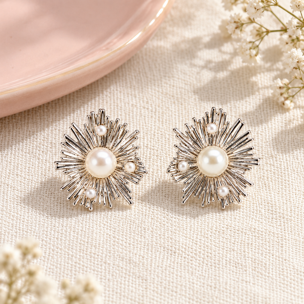 Silver starburst pearl stud earrings resting on an ivory linen background next to a blush pink tray.