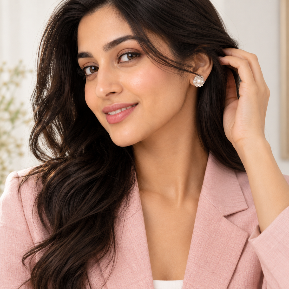 Three-quarter view of a woman tucking her hair back to display a silver pearl stud earring.