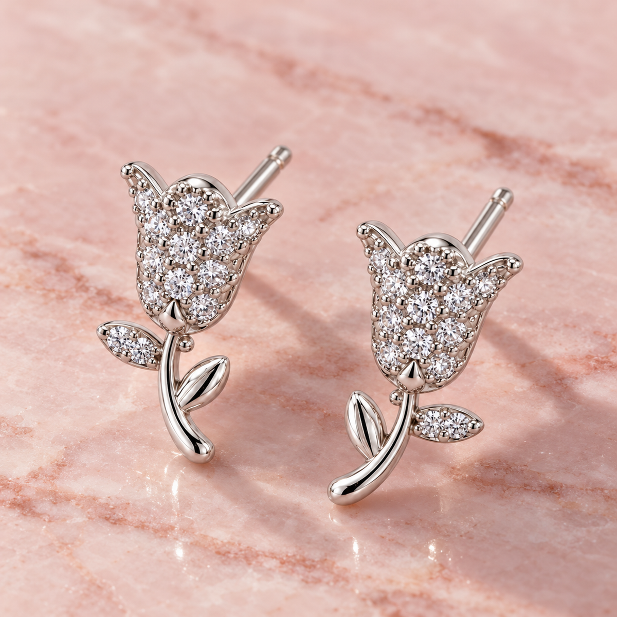Tulip stud earrings resting on a smooth blush pink marble surface.