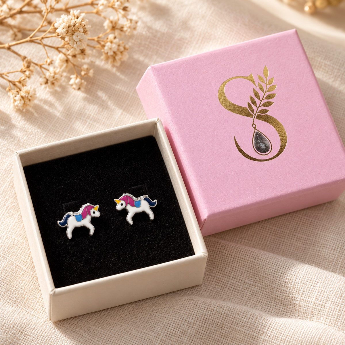 Silver unicorn stud earrings presented inside an open pink gift box with black velvet lining.