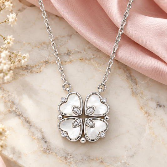 Silver and mother of pearl clover necklace on an ivory marble surface with soft blush pink silk fabric.