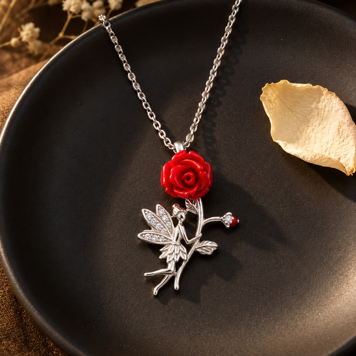 Silver fairy and rose necklace draped on a matte black plate with a single ivory petal under soft side light.