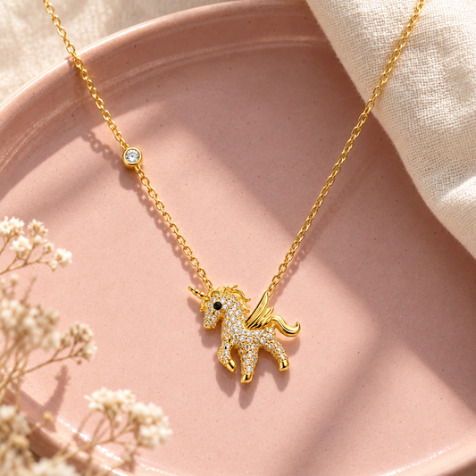 Gold unicorn pendant necklace resting on a blush pink tray with linen fabric.