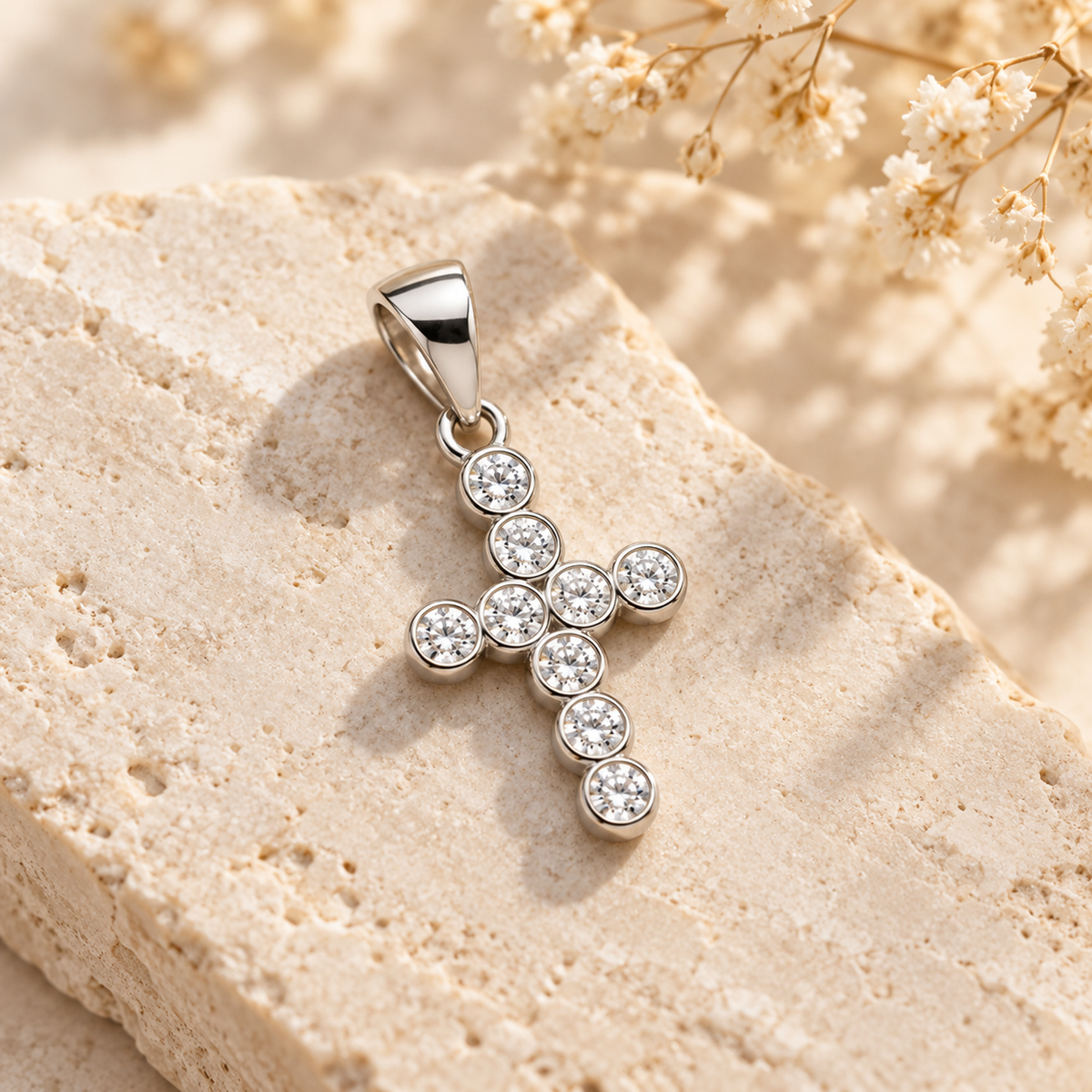 Silver bezel-set cross pendant resting gracefully on an ivory stone slab in soft sunlight.