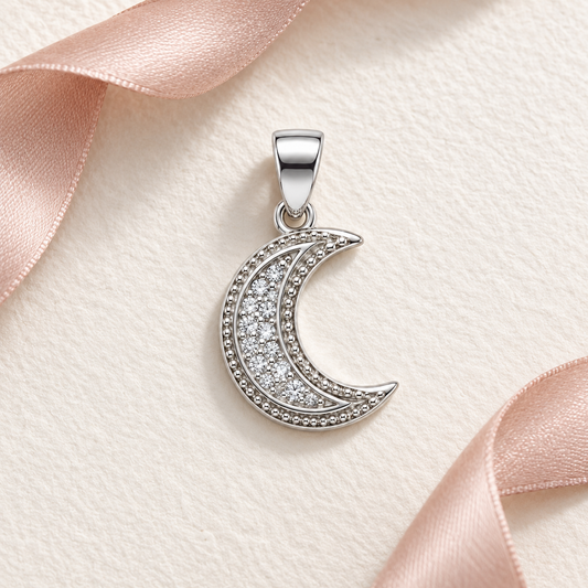 Silver crescent moon pendant resting on ivory paper next to blush pink ribbon.