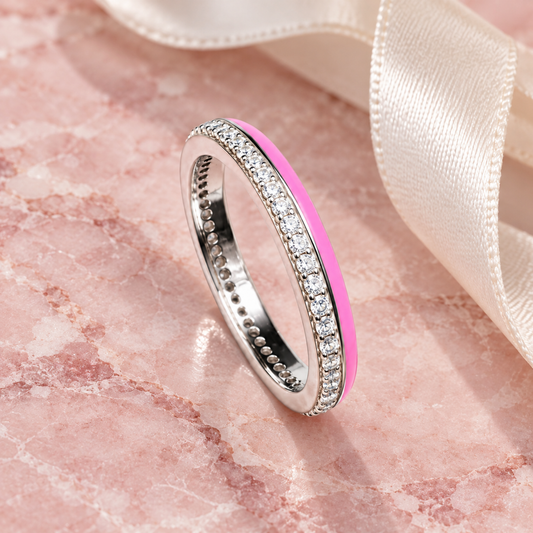 Silver ring with pink enamel detail lying on blush pink marble alongside an ivory ribbon.