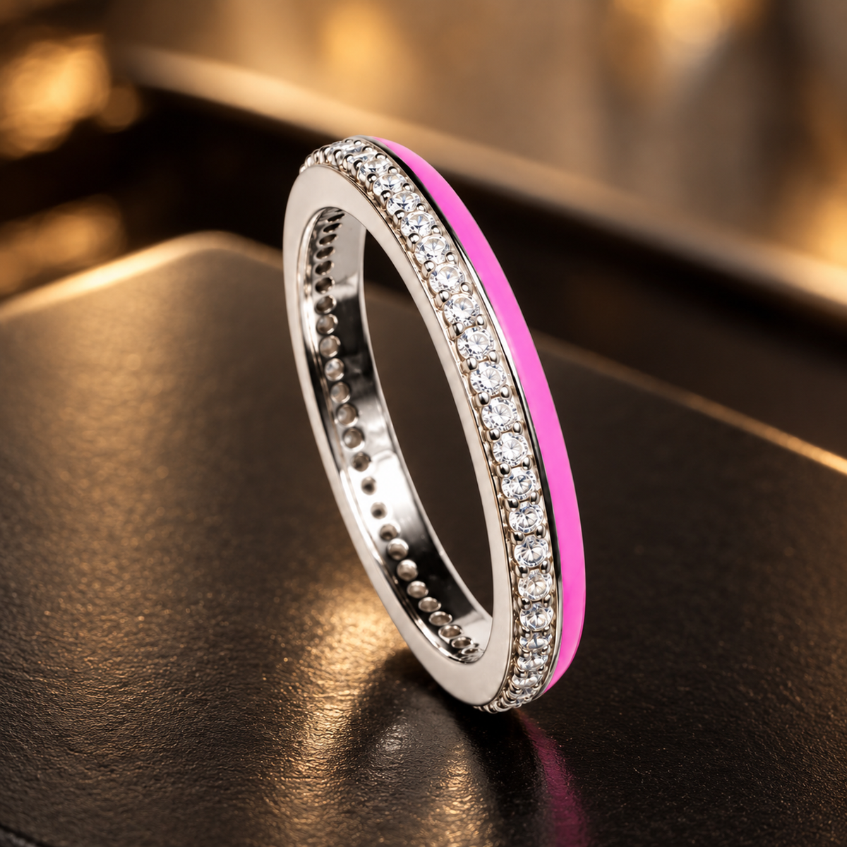 Silver cubic zirconia and pink enamel band ring displayed on a dark matte ceramic surface.