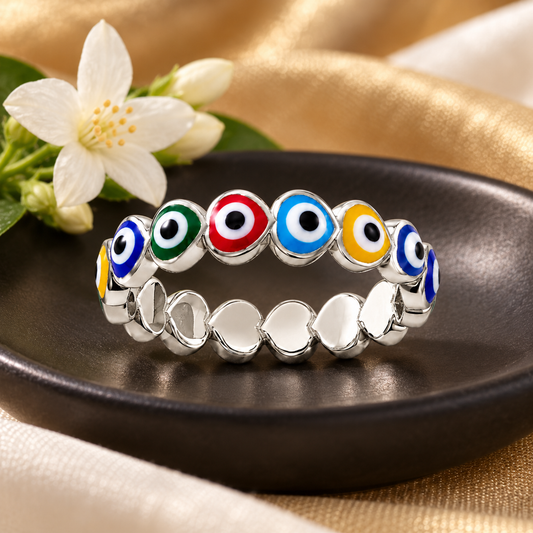 Sterling silver heart ring with colourful enamel details resting on a black ceramic dish with jasmine flowers.