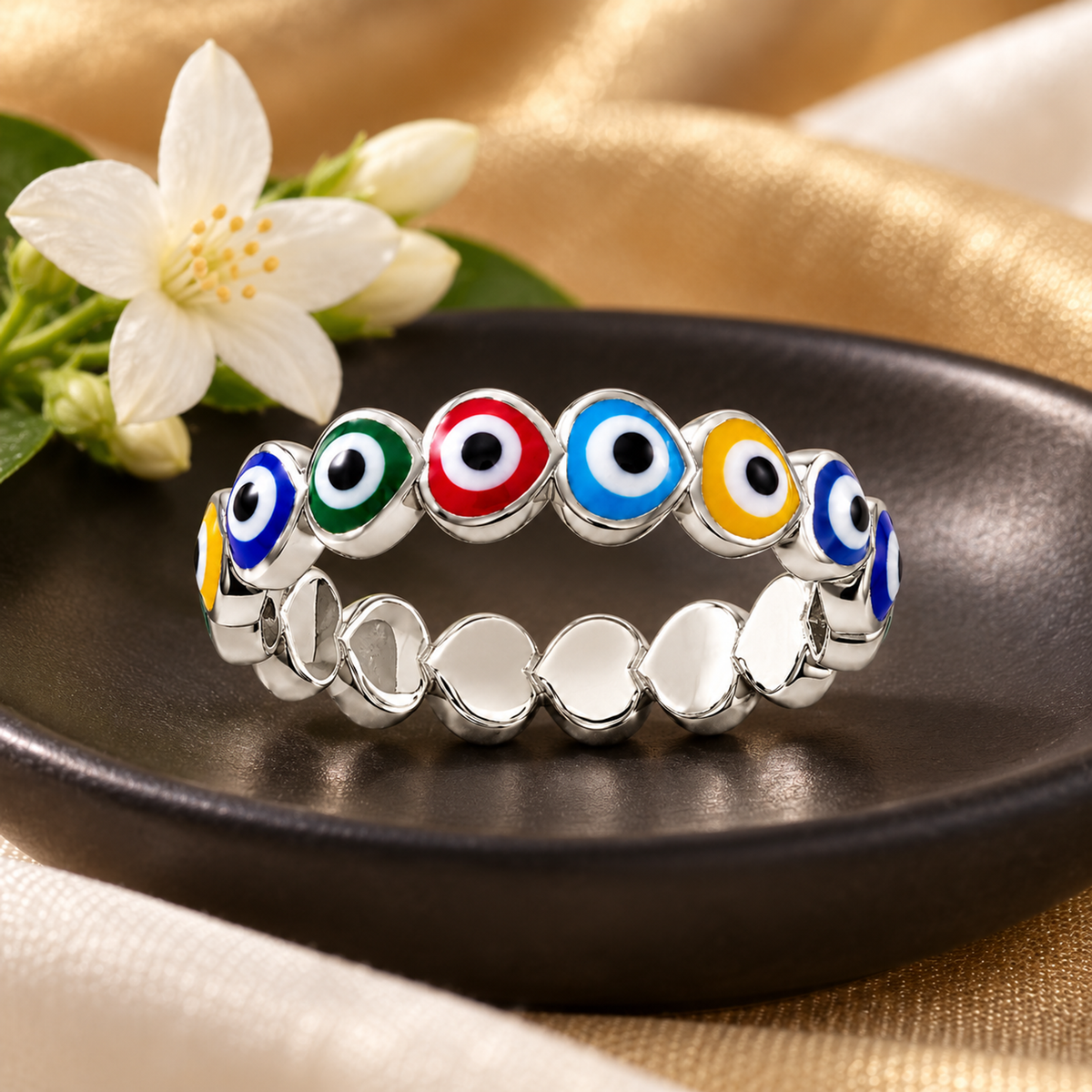 Sterling silver heart ring with colourful enamel details resting on a black ceramic dish with jasmine flowers.