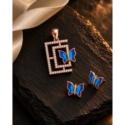 Butterfly pendant and studs on black slate beside a curl of ivory silk ribbon.