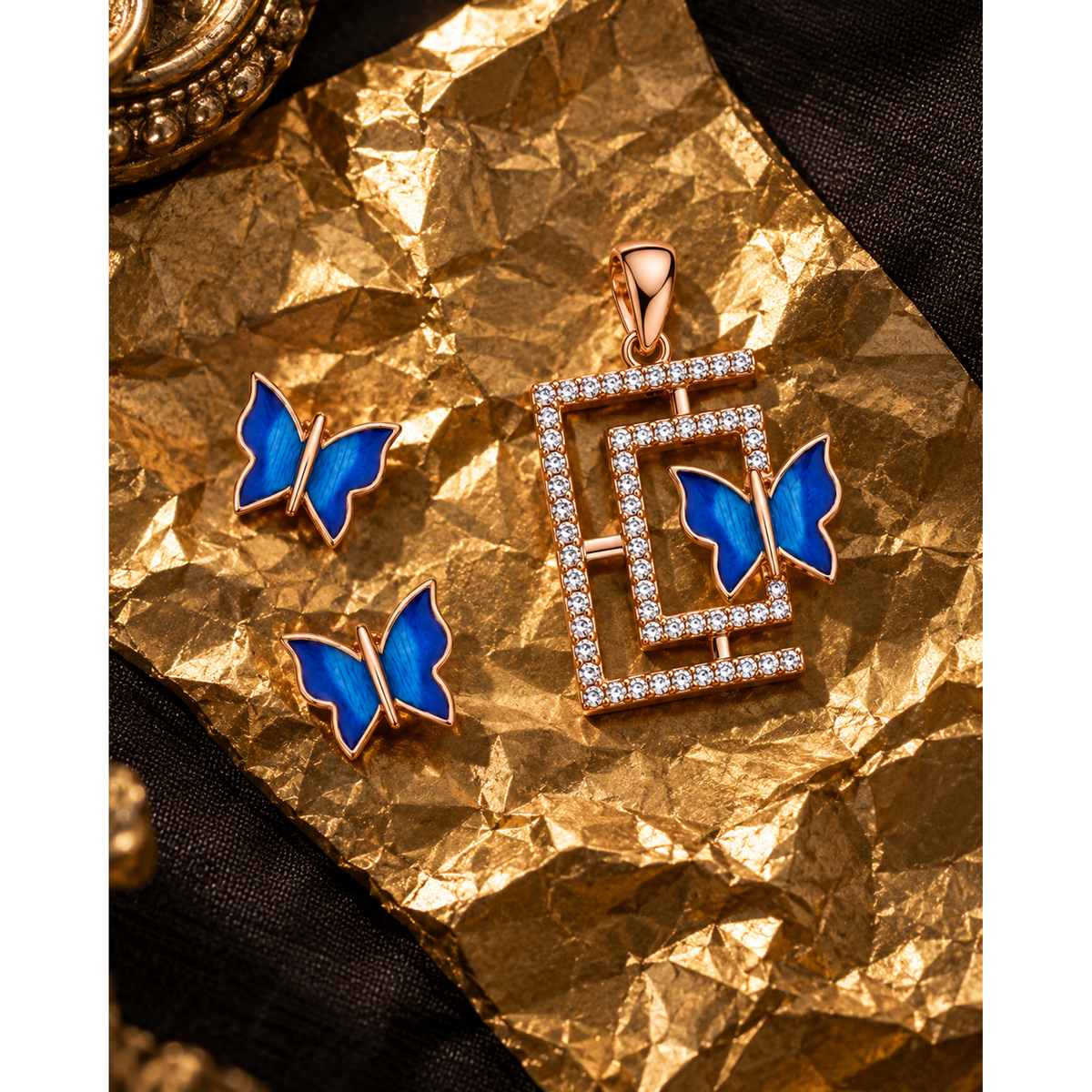 Butterfly pendant and two studs arranged on crumpled gold foil over dark linen.