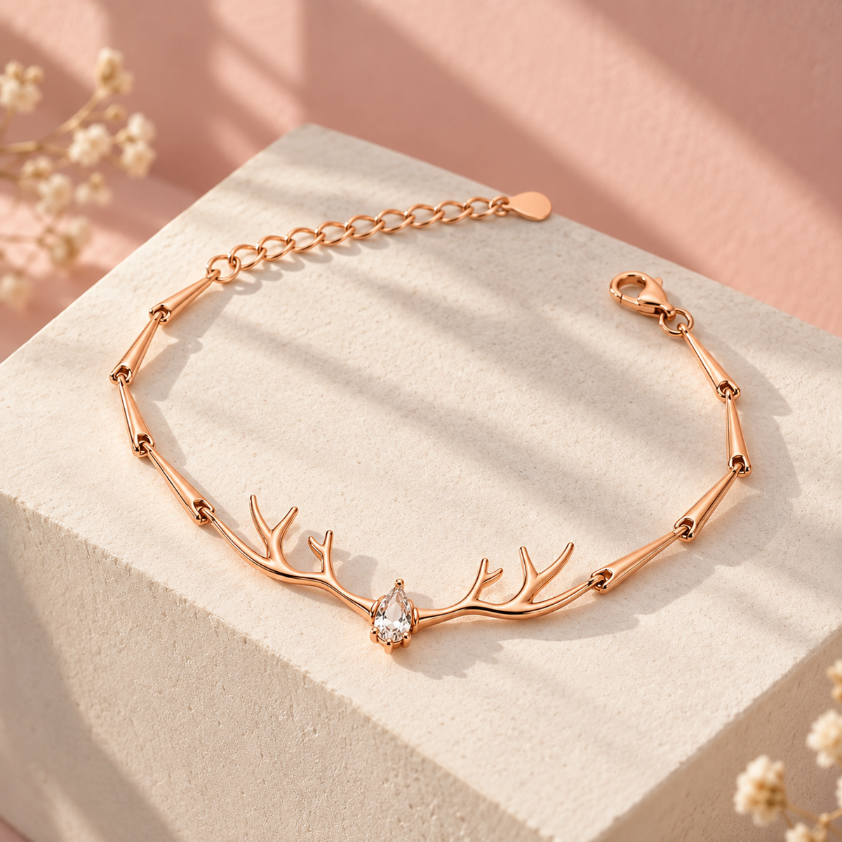 Rose gold antler bracelet displayed on an ivory pedestal against a blush pink background.