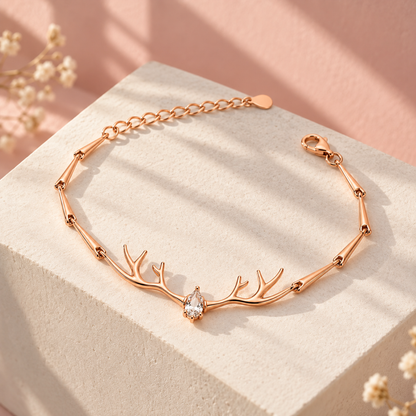 Rose gold antler bracelet displayed on an ivory pedestal against a blush pink background.