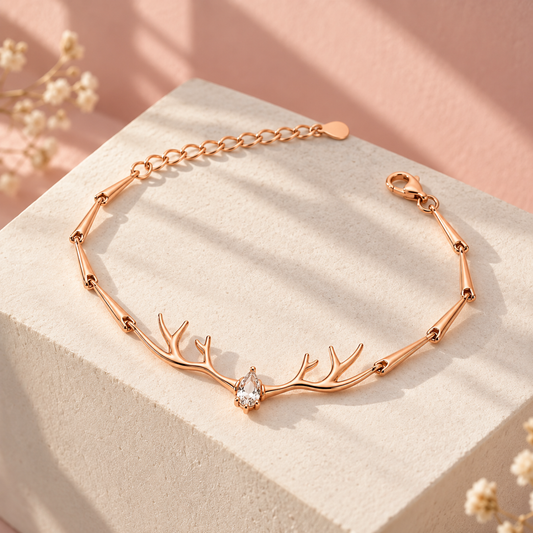 Rose gold antler bracelet displayed on an ivory pedestal against a blush pink background.