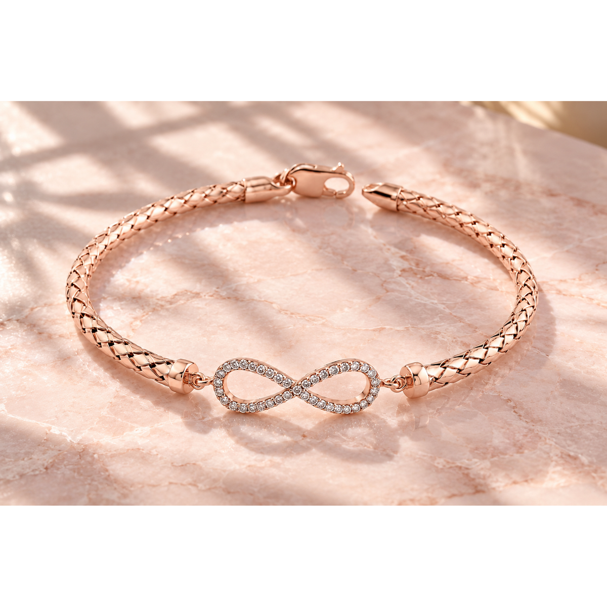 Rose gold mesh infinity bracelet resting on smooth blush pink marble in natural morning sunlight.
