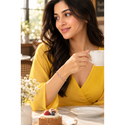 Close-up of woman holding a teacup, wearing a delicate rose gold woven infinity bracelet.