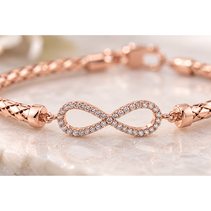 Macro detail of pave cubic zirconia infinity emblem on rose gold woven mesh bracelet.