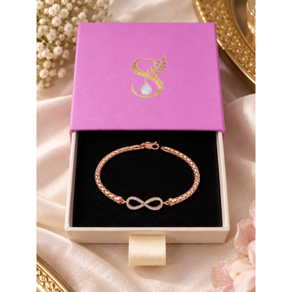 Rose gold infinity bracelet displayed inside open Silvanya magenta drawer gift box on black velvet.