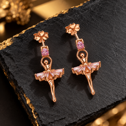 Ballerina drop earrings displayed on a matte black slate surface with warm lighting.