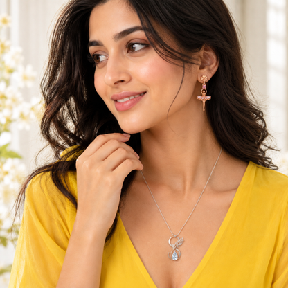 Frontal shot of a woman wearing ballerina drop earrings with a pink off-shoulder knit top.