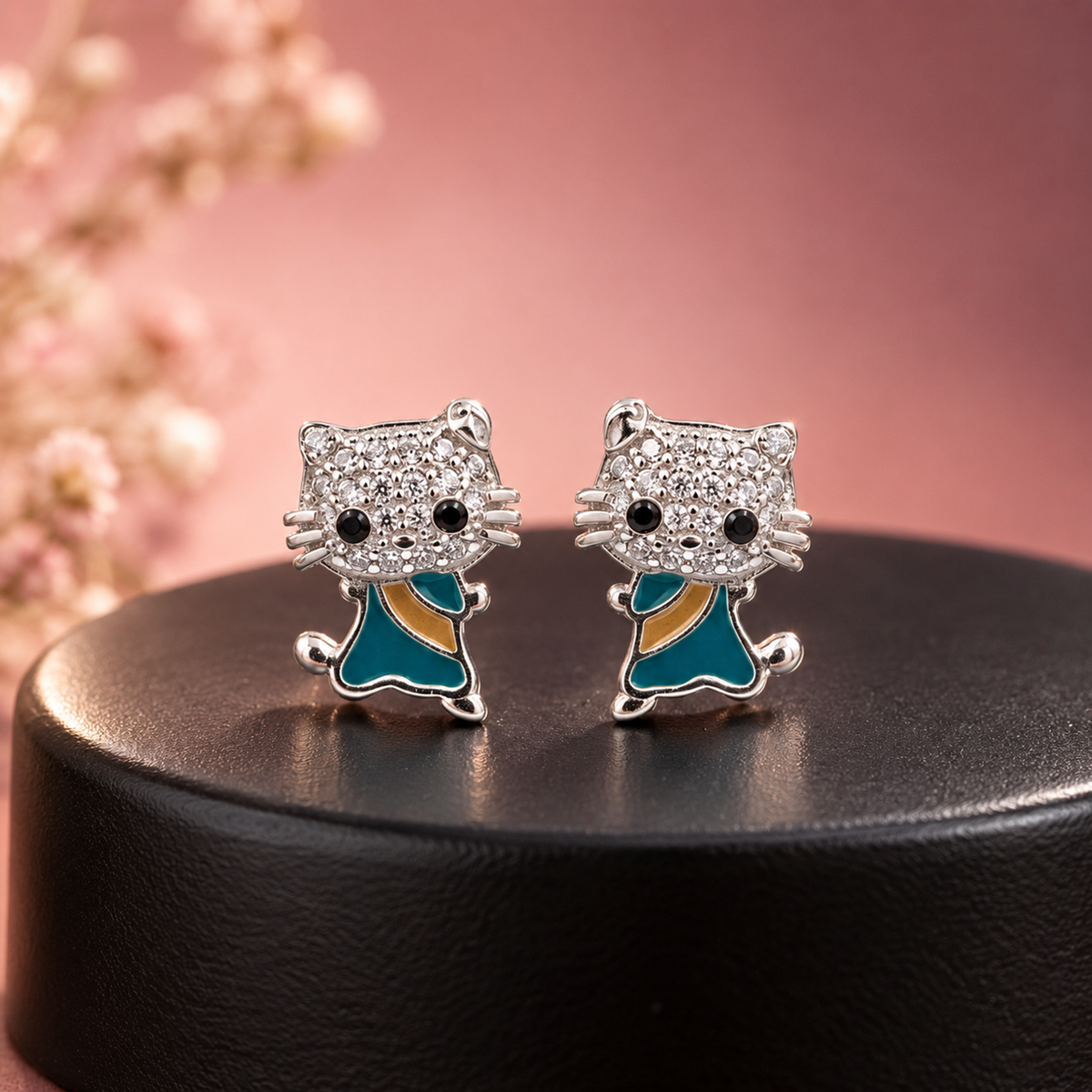 Silver cat studs resting on a matte black ceramic pedestal with soft pink background.