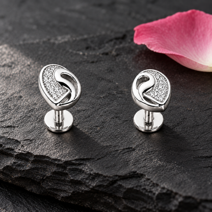Clover silver stud earrings on a dark slate stone next to a delicate pink petal.