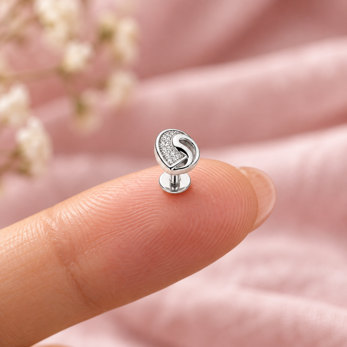 A tiny 4mm silver clover earring resting on a fingertip to show its scale.