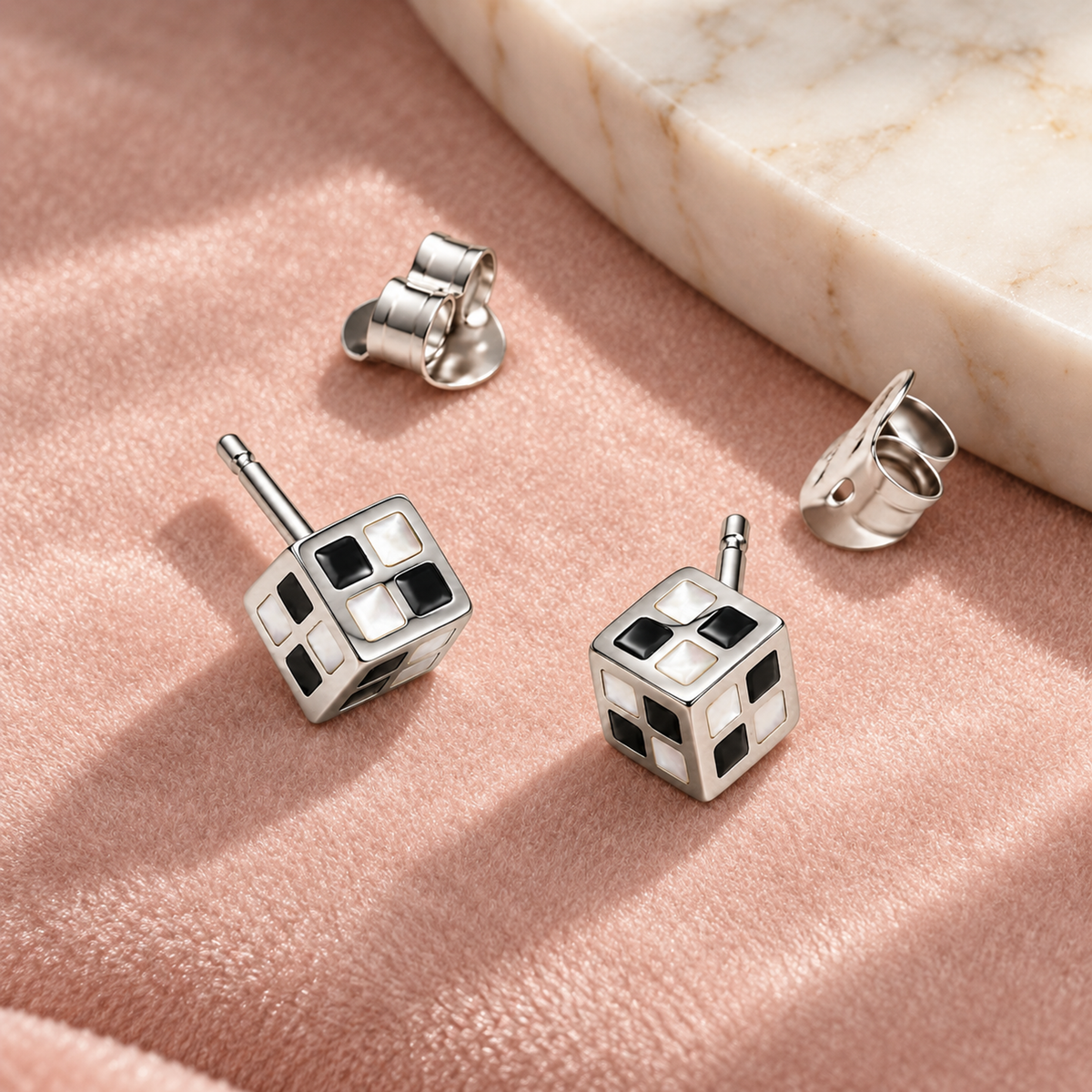 Monochrome cube stud earrings on blush pink velvet near an ivory marble tray.