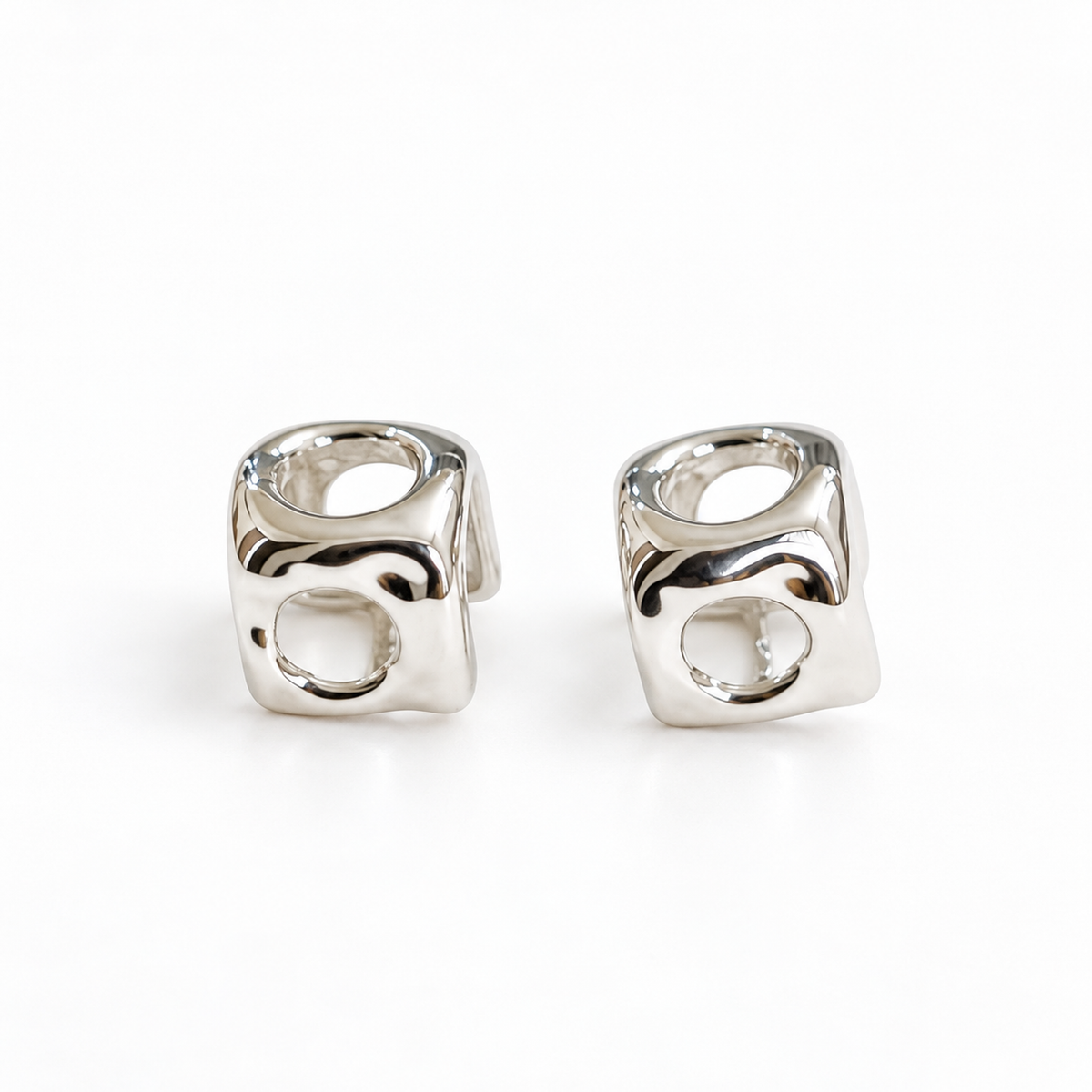 A pair of high-polish silver cube stud earrings with openwork circular cutouts on a pure white background.