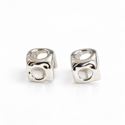 A pair of high-polish silver cube stud earrings with openwork circular cutouts on a pure white background.