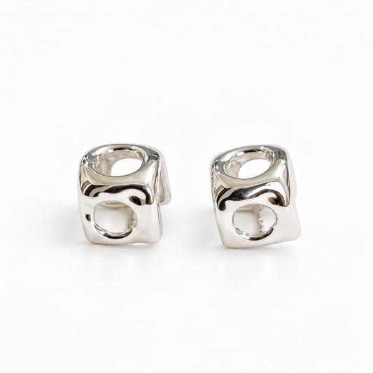 A pair of high-polish silver cube stud earrings with openwork circular cutouts on a pure white background.