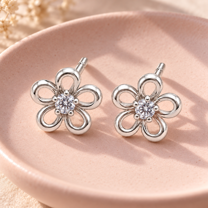 Silver flower stud earrings resting on a pale blush pink ceramic dish.