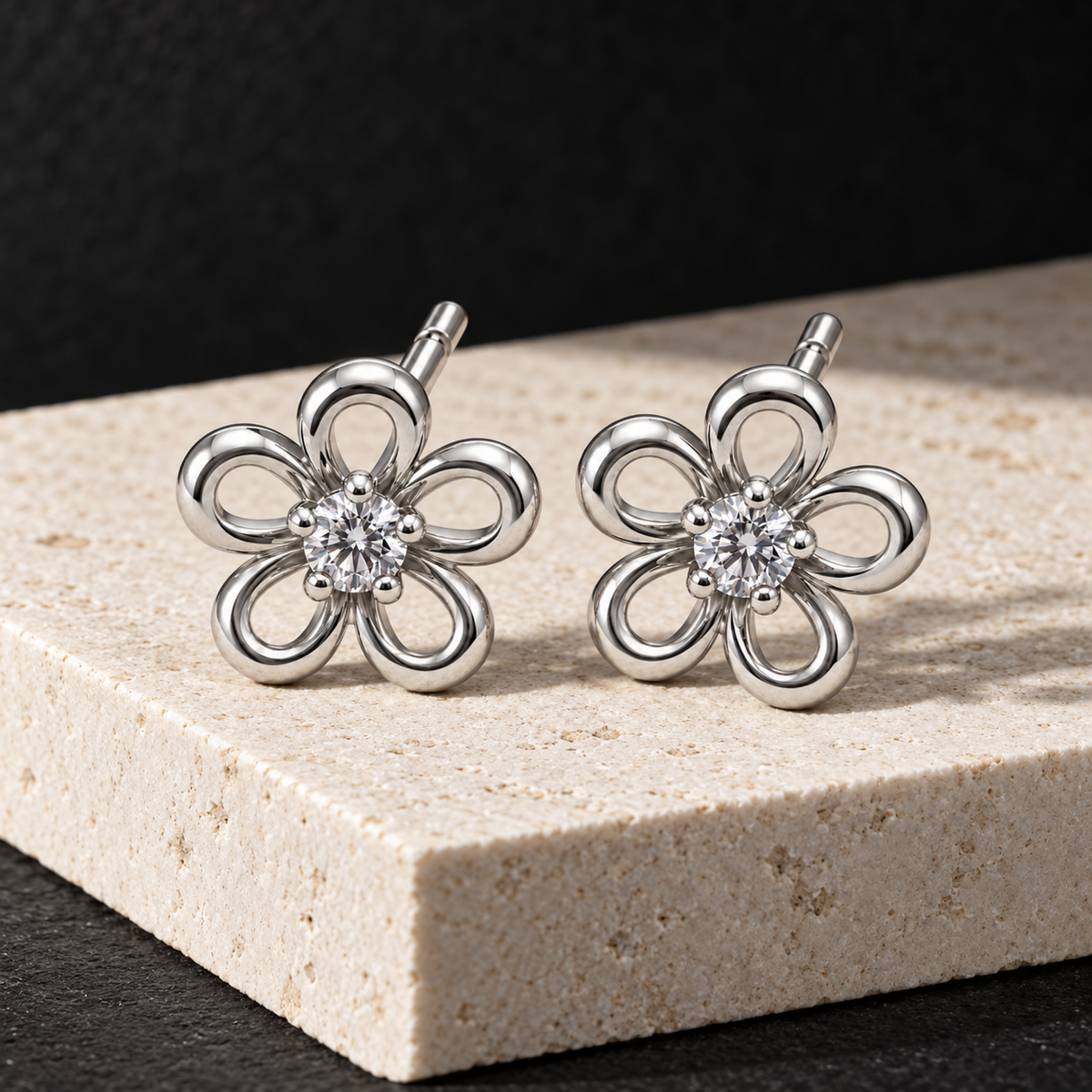 Silver flower studs placed on an ivory limestone slab with a matte black backdrop.