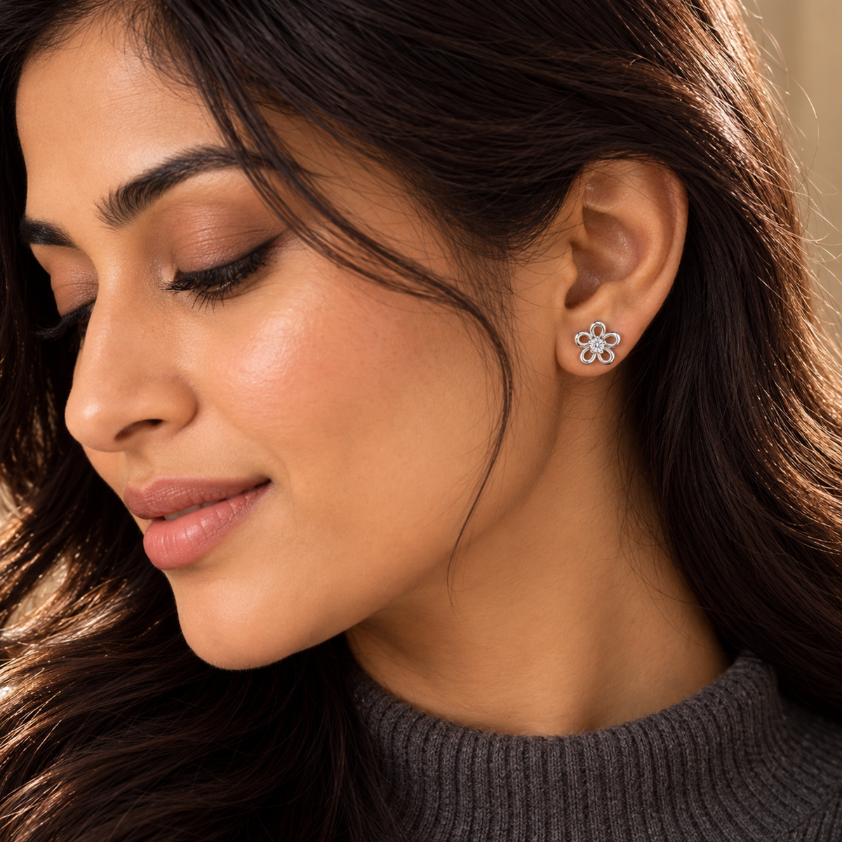 Close-up of a woman's ear wearing a silver floral stud earring with eyes gently closed.