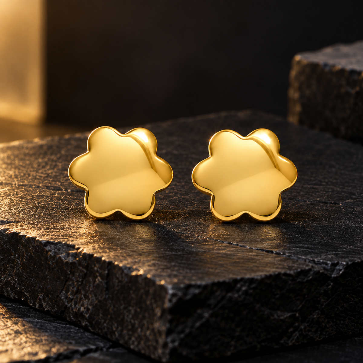 Gold blossom stud earrings resting on a matte black slate pedestal.