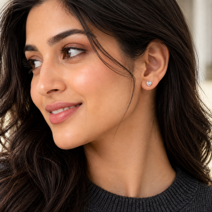 Woman wearing small silver heart stud earrings in her earlobe.
