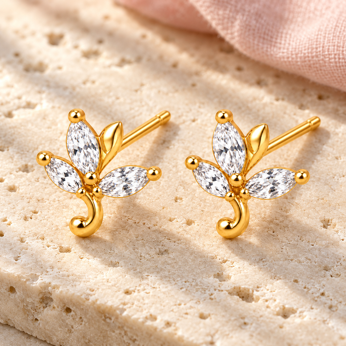 Gold botanical stud earrings resting on an ivory stone tray in morning light.