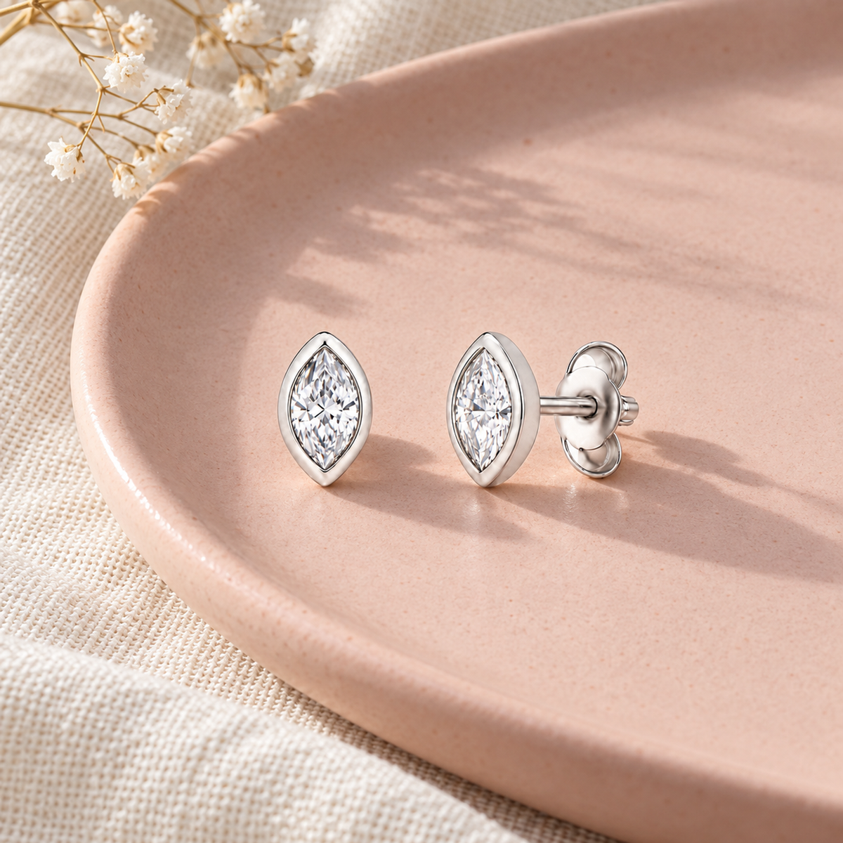 Silver marquise studs placed on a light pink tray with folded ivory linen.