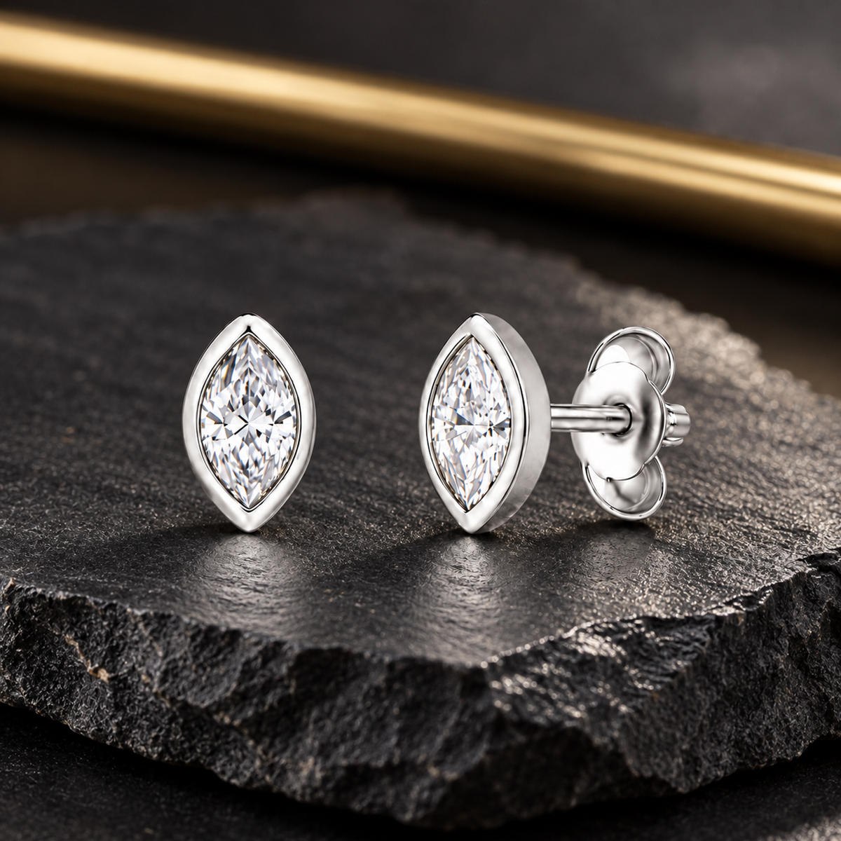 Silver stud earrings on a dark textured slate background with subtle gold accents.