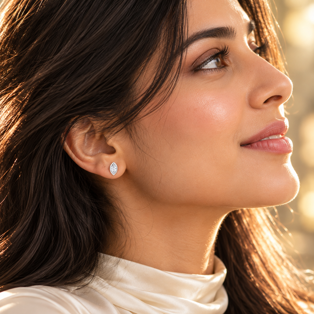 Close-up profile of a woman wearing a sparkling silver marquise stud earring in warm light.
