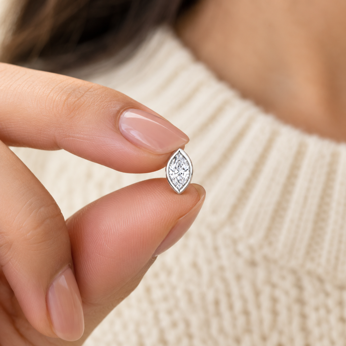 A tiny marquise silver earring held gently between fingers to show its small size.