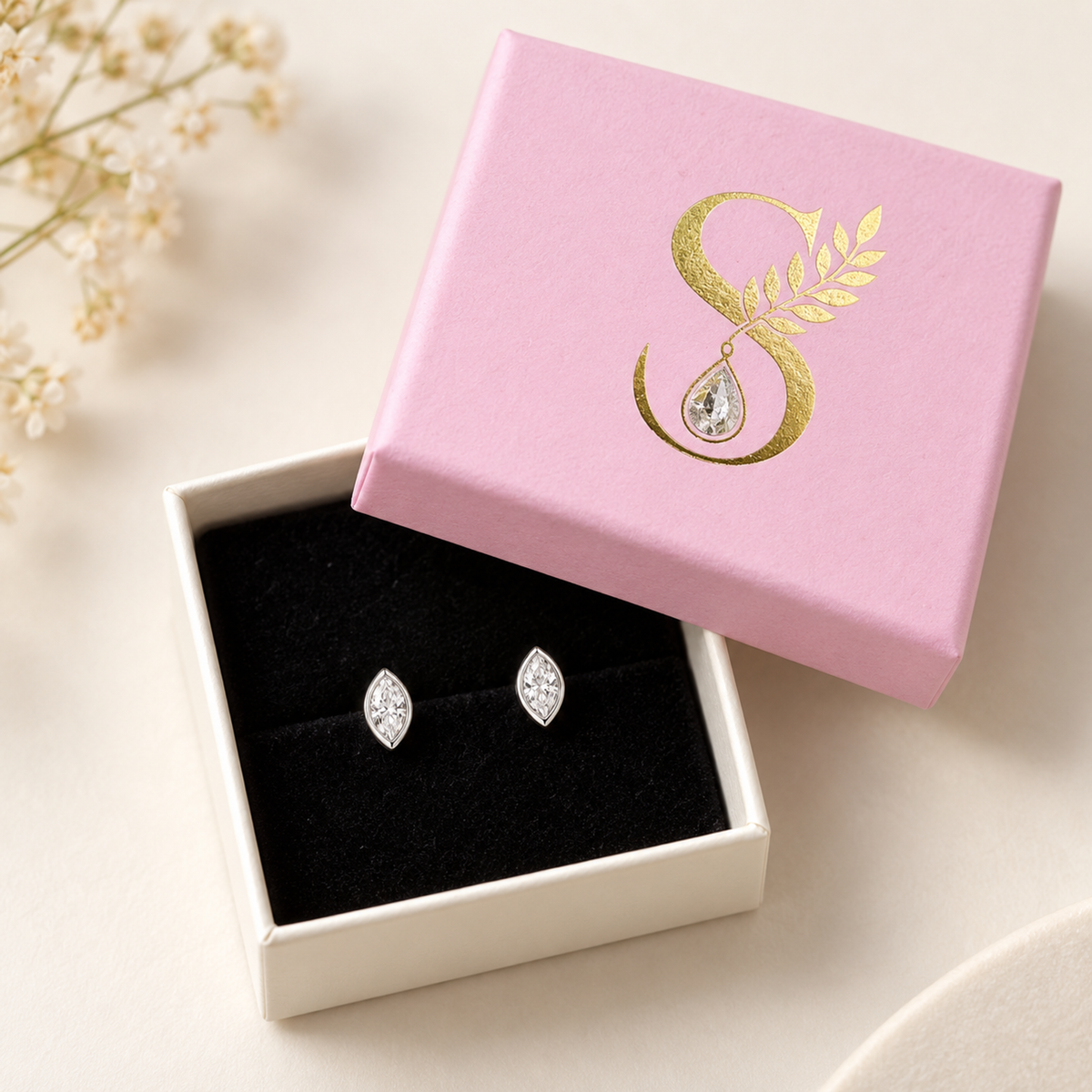 Pair of silver studs displayed inside an open pale pink gift box with black velvet lining.